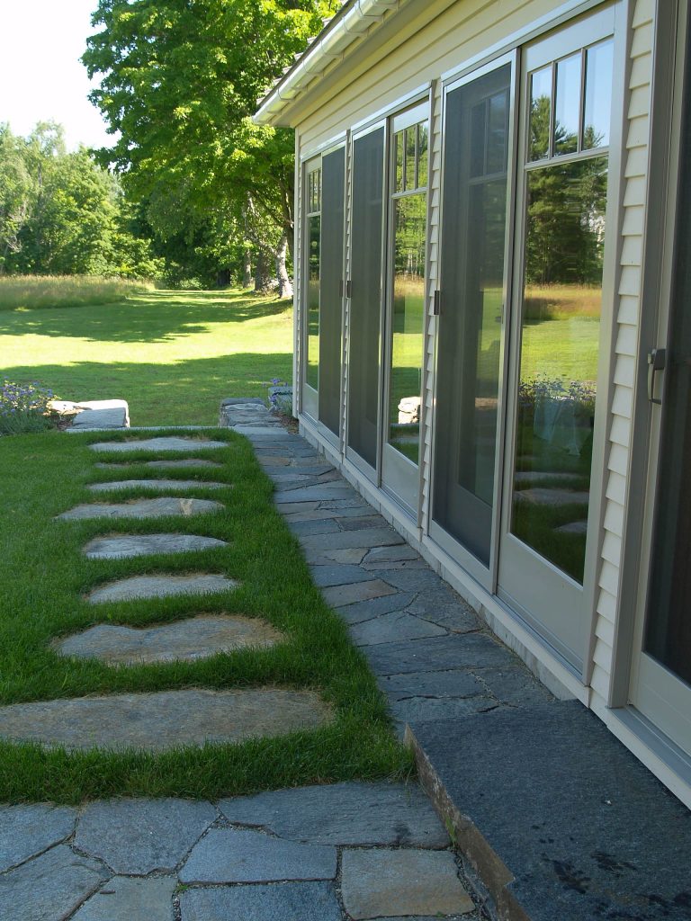 Simple detailed stone elements extend the porch's craftsmanship out into the landscape, and are reflected in the glass doors. Scott Wunderle