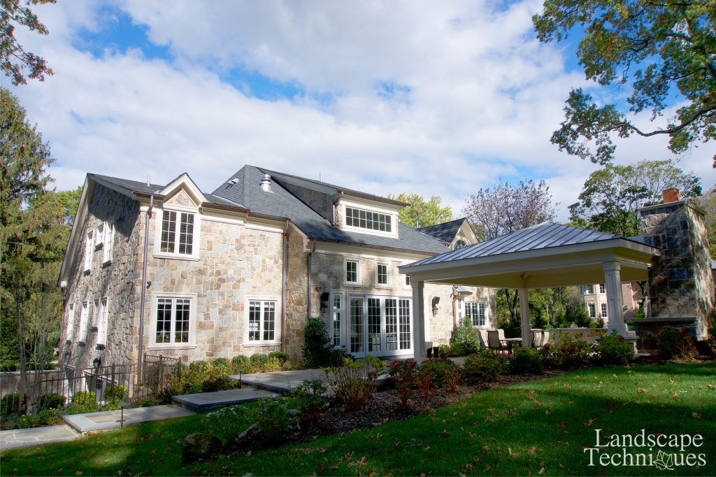 Stone faced home with entry gates and piers. Rear yard includes pergola, patio and fire pit area for entertaining. Landscape & Design by Landscape Techniques.