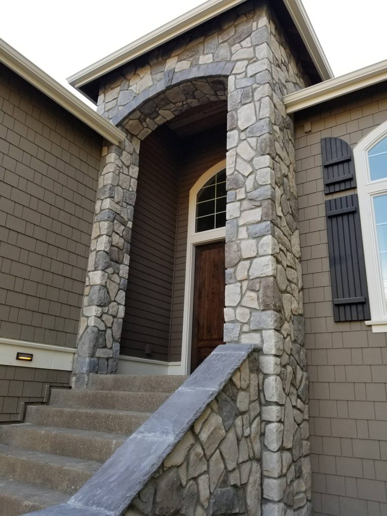 Stone veneer at entry of home, utilizing a field stone type cultured stone and stone cap accent over arch.