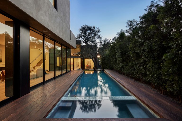 At spa edge with swimming pool and surrounding raised Thermory wood deck framing the Oak tree beyond. Lawn retreat below. One can discern the floor level change created by following the natural grade slope of the property: Between the Living Room on left and Gallery / Study on right. Photo by Dan Arnold by Hsu McCullough | Pool design | Pool Contracting | Swimming Pool Ideas | Swimming Pool Design Ideas