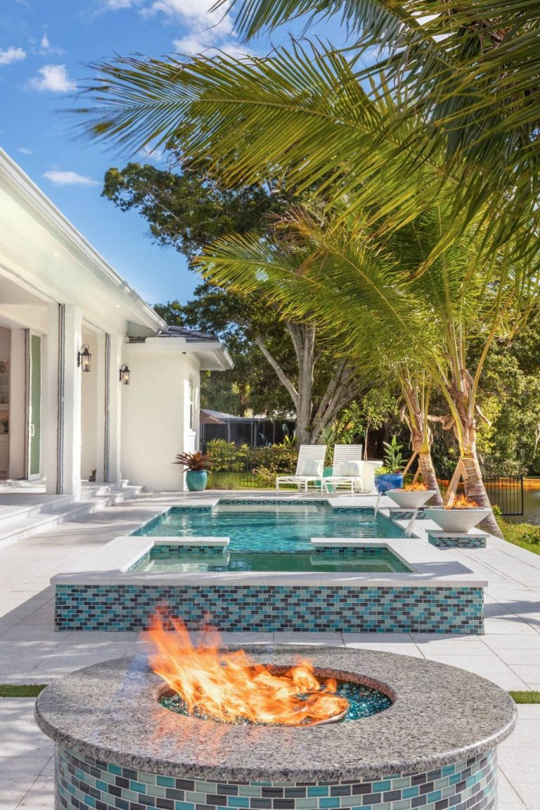 Stunning linear custom swimming pool, spa and outdoor fireplace surrounded by white custom pavers with Florida and oyster shells.