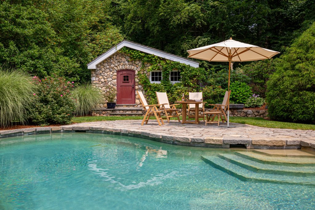 Teak chairs that do double duty as dining chairs but also recline play off the natural elements in this pool set-up straight out of Harry Potter Casting.