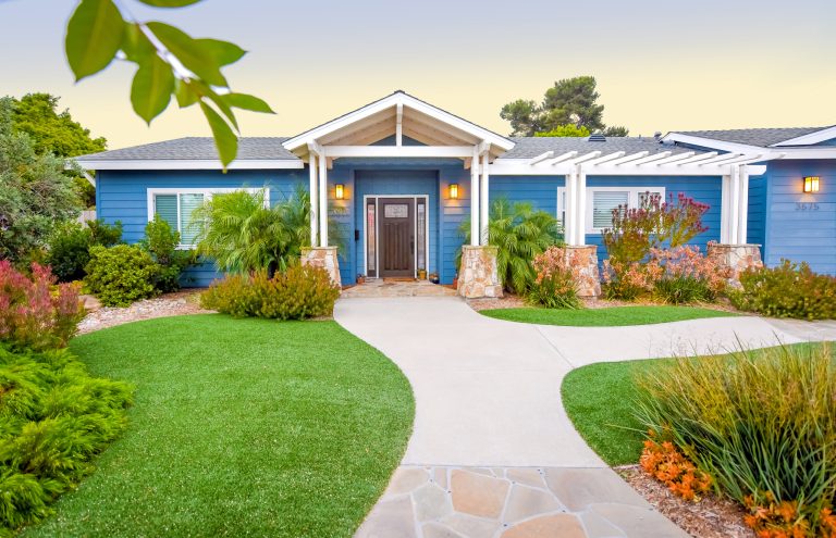 The front yard and entry walkway is flanked by soft mounds of artificial turf along with a mosaic of orange and deep red hughes within the plants. Designed and built by Landscape Logic.