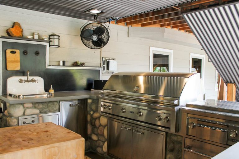 The outdoor kitchen boasts a large and beautiful range and other stainless appliances, as well as a vintage farm sink. Concrete countertops and stone siding match interior finishes throughout the home.