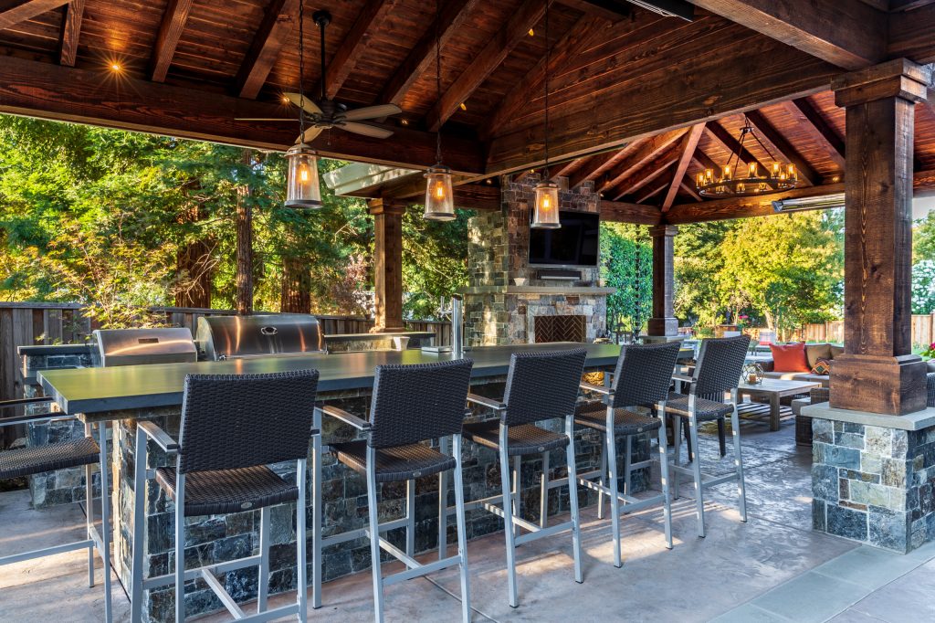 The outdoor kitchen is equipped with a ceiling fan and pendant lights to ensure that practicality also accompanies style.