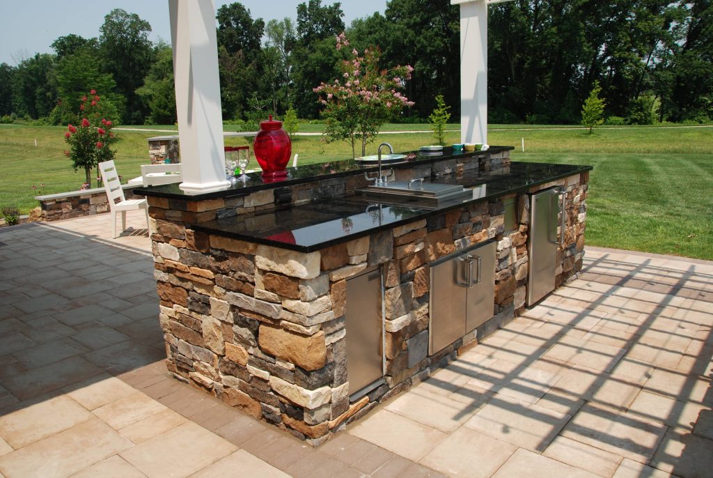 The stone veneer and granite excellently conceal the more practical parts responsible for bringing the utilities out to this kitchen. The pergola provides shade right where it is needed.