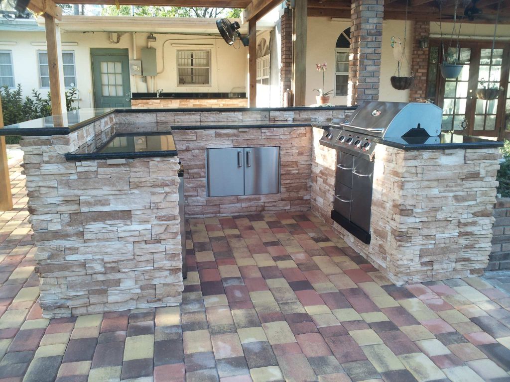 This "U" shape outdoor kitchen with raised Bar, stacked stone and dark granite over paver flooring is an amazing way to complement your beautiful backyard when you have a smaller patio.