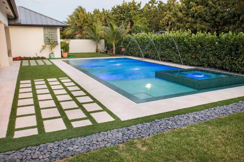 This beautiful pool in Miami Florida features one of a kind landscaping with spa and wet edge! The tile for the pool and spa are beautiful teal colors and the LED lights add extra flavor at night!