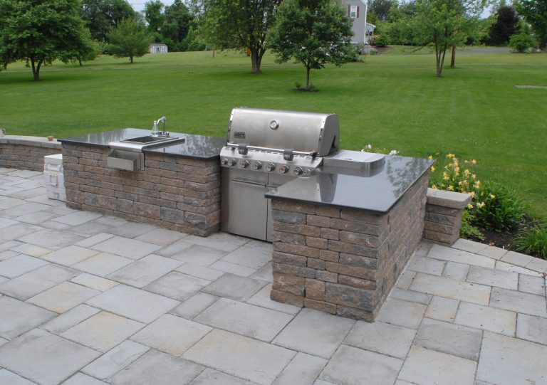 This built-in grill and stainless steel sink make for a beautiful outdoor kitchen and entertaining space that overlooks the manicured lawn and landscaped garden beds.