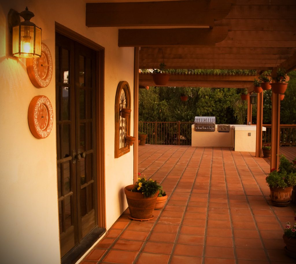This covered patio uses cedar wood, Spanish tile and stucco. This path leads to a built in barbecue and food prep area. Black french doors add to the rustic nature of this backyard remodel.
