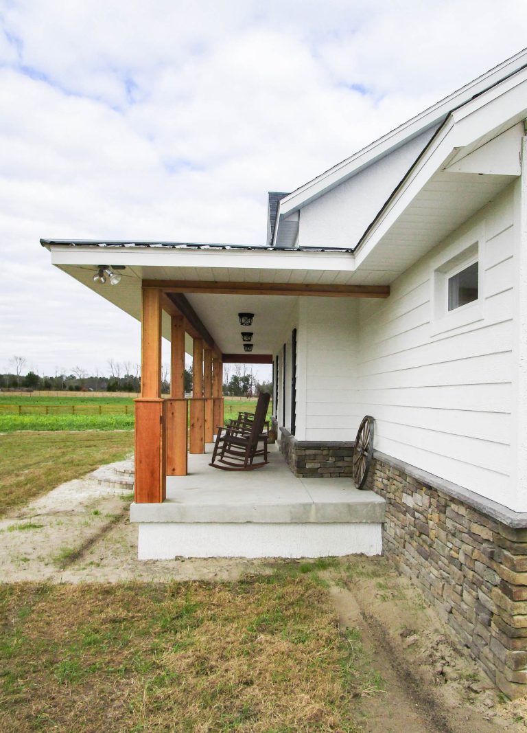 This is a custom farmhouse style home in Ocala, Florida with a large front porch, cedar wood columns, white lap siding, and stone work.