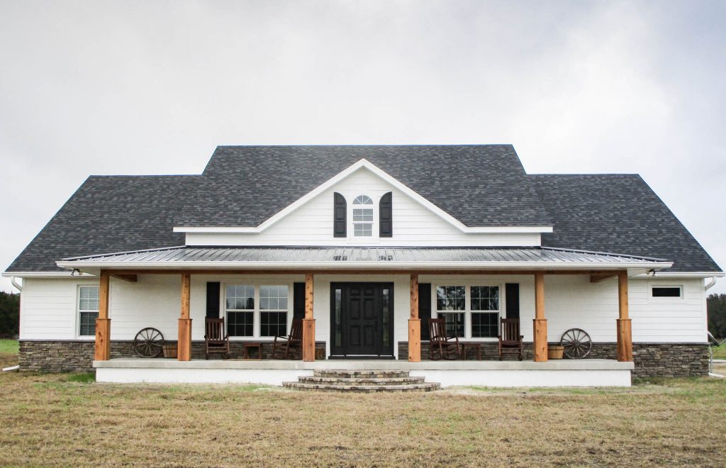 This is a custom farmhouse style home in Ocala, Florida with a large front porch, cedar wood columns, white lap siding, and stone work.