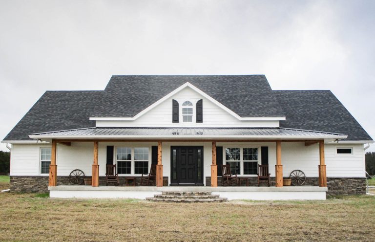 This is a custom farmhouse style home in Ocala, Florida with a large front porch, cedar wood columns, white lap siding, and stone work.