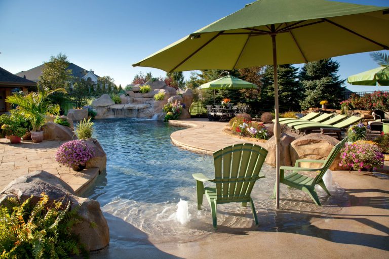 This lagoon swimming pool features a vanishing edge, rock waterfall, slide, beach entry with rock accents, water geysers and a large travertine patio Shehan Pools
