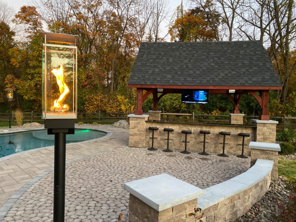 This project features an in ground pool, paver patio and walkway, roof structure, outdoor bar area, seat wall, columns, outdoor lighting, landscape lighting and fire lamps.
