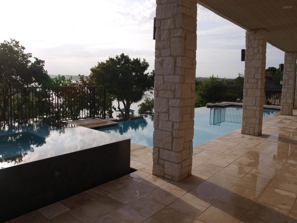 This vanishing edge pool with a perimeter overflow spa enhances the beatiful view of the lake. The travertine coping blends well with the limestone columns and will withstand the salt water of the pool.