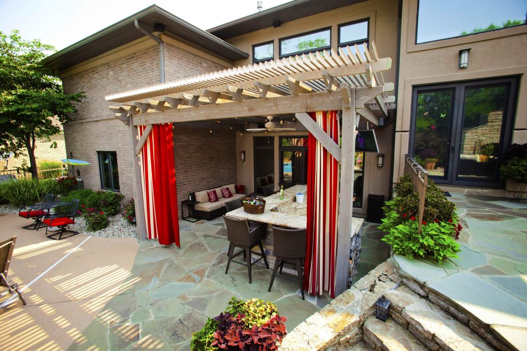 Timber frame attached pergola kit with a louvered open and close roof to let in some sunshine or close off for shade or the rain. Privacy curtains were added with an outdoor bar and seating.