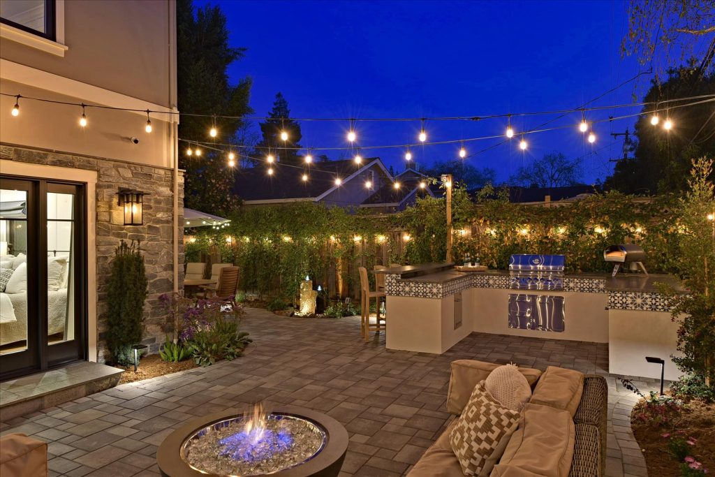 Tucked in the rear corner of the yard, the outdoor kitchen connects the side patio with its dining area with the rear patio and lounge area. A fire table provides warmth on cool California evenings.