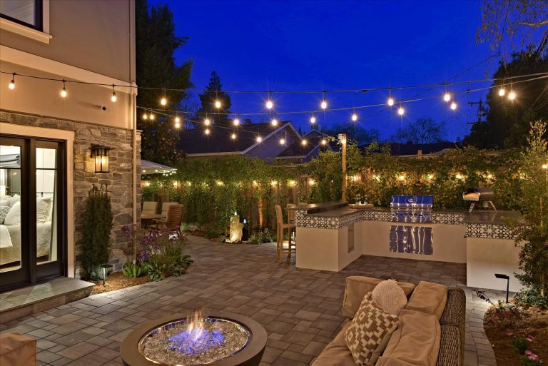 Tucked in the rear corner of the yard, the outdoor kitchen connects the side patio with its dining area with the rear patio and lounge area. A fire table provides warmth on cool California evenings.