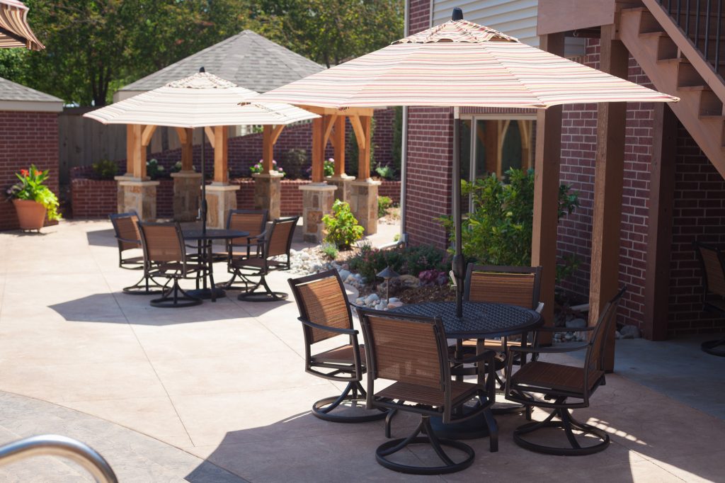 Two casual dining and gathering spaces line the pool and are shaded with patio umbrellas. It's the perfect spot to grab a quick bite while watching the fun in the pool. by All Things Barbecue | Outdoor Kitchens | Backyard Design | Outdoor Living Spaces | Landscape Design