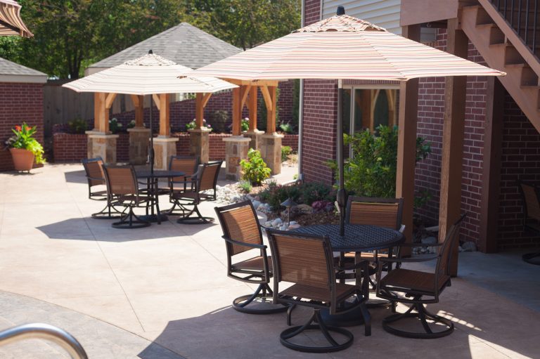 Two casual dining and gathering spaces line the pool and are shaded with patio umbrellas. It's the perfect spot to grab a quick bite while watching the fun in the pool. by All Things Barbecue | Outdoor Kitchens | Backyard Design | Outdoor Living Spaces | Landscape Design