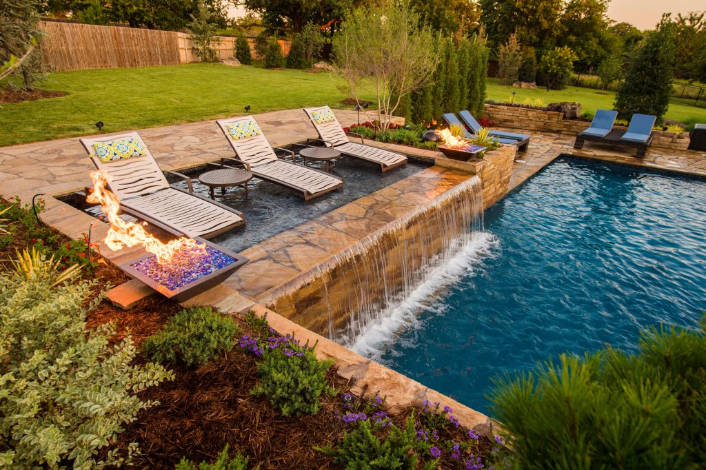 View of the glass tiled sun shelf with fire pots framing the spill over water feature into the pool. Design and construction by Caviness Landscape Design Photography by KO Rinearson