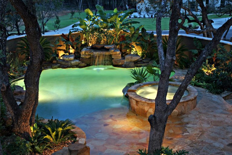 Waterfall, spa and beach entry at night with LED pool lighting.