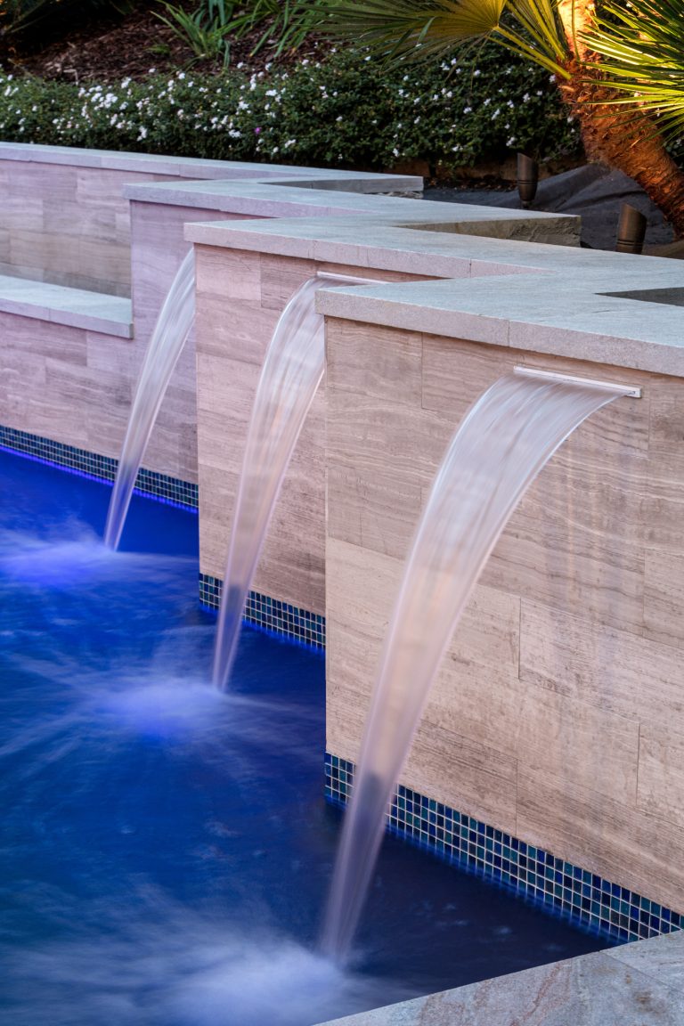 Waterfalls under White quartzite 5cm eased edge coping, Marble tiled walls with glass mosaic waterline tile and midnight blue mini pebble pool finish WOW by Distinguished Pools | Pool design | Pool Contracting | Swimming Pool Ideas | Swimming Pool Design Ideas