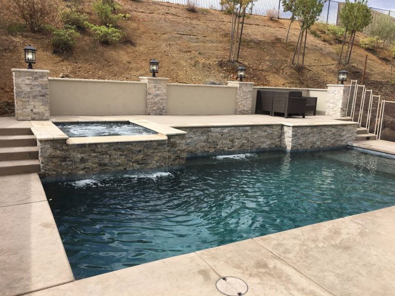 With an ascending slope, we were able to tuck this pool and spa into the hillside and maximize their outdoor space. We used travertine for coping on the upper edge of the raised bond beam and tie that into the pool using a split faced travertine on the face and highlighted columns