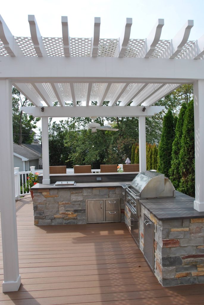 a custom outdoor kitchen equipped with Lynx Grill, side burner, storage and accessories. Covered with an azek pergola and illuminated with Cast brand LED niche lights.