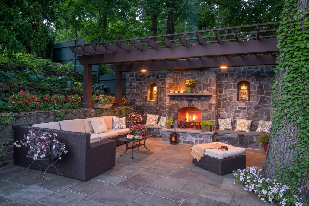 Like most growing families, this client wanted to lure everyone outside. And when the family went outdoors, they were hoping to find flamboyant color, delicious fragrance, freshly grilled food, fun play-spaces, and comfy entertaining areas waiting. Privacy was an imperative. Seems basic enough. But a heap of challenges stood in the way between what they were given upon arrival and the family's ultimate dreamscape.

Primary among the impediments was the fact that the house stands on a busy corner lot. Plus, the breakneck slope was definitely not playground-friendly. Fortunately, Westover Landscape Design rode to the rescue and literally leveled the playing field. Furthermore, flowing from space to space is a thoroughly enjoyable, ever-changing journey given the blossom-filled, year-around-splendiferous gardens that now hug the walkway and stretch out to the property lines. Soft evergreen hedges and billowing flowering shrubs muffle street noise, giving the garden within a sense of embrace. A fully functional (and frequently used) convenient outdoor kitchen/dining area/living room expand the house's floorplan into a relaxing, nature-infused on-site vacationland. Mission accomplished. With the addition of the stunning old-world stone fireplace and pergola, this amazing property is a welcome retreat for year round enjoyment. Mission accomplished.

Rob Cardillo for Westover Landscape Design, Inc. by Westover Landscape Design | Fire Pits|Backyard Design|Outdoor Living Spaces|Landscape Design|Backyard Ideas|Landscaping|Landscaping Ideas|Landscape Installation|Fire Feautures|Fire Pit