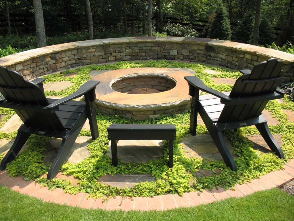 A circular firepit surrounded by an informal patio consisting of widely spaced irregular flagstones with Creeping Jenny (Lysimachia nummularia 'Aurea') growing between them, and a semi-circular fieldstone sitting wall at the back. This was designed and built by Outdoor Expressions with the help of a former employee of ours.