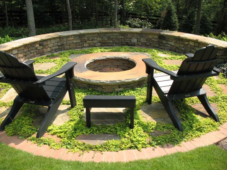 A circular firepit surrounded by an informal patio consisting of widely spaced irregular flagstones with Creeping Jenny (Lysimachia nummularia 'Aurea') growing between them, and a semi-circular fieldstone sitting wall at the back. This was designed and built by Outdoor Expressions with the help of a former employee of ours.