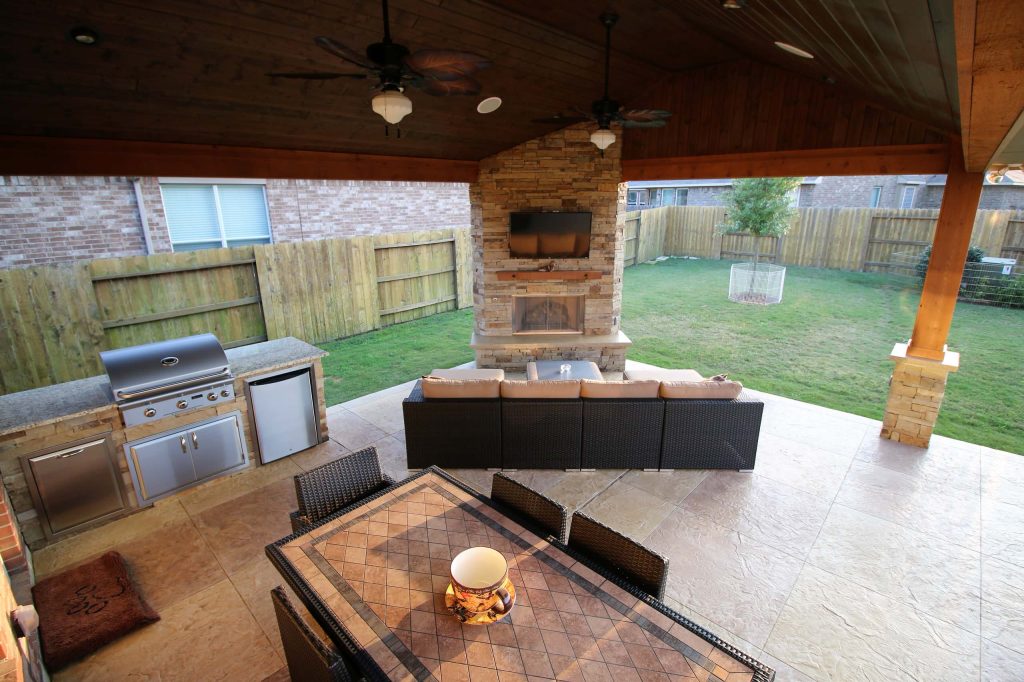 This project included a Patio Cover Addition, Outdoor Kitchen, Gas-Burning Fireplace, and Stamped Concrete walking surface with a custom pattern. The attention is immediately drawn to the Ledgestone fire place with a rustic cedar mantel. The Ledgestone flows continuously throughout the space, found on the base of the patio columns and outdoor kitchen. The kitchen sparkles with Stainless Steel appliances, containing storage compartments, refrigerator, and grill. Topped with Venetian Gold Granite, this cooking space provides ample counter space that is easily maintained. The overall appeal of this Outdoor Living area remains beautifully traditional, with cedar-trimmed columns and beams. Also, though it has custom features, this addition is built to look original to the home with matching paint, shingles, gutters, and framing materials. The elaborate, pre-stained Tongue and Groove ceiling is quite an attractive feature to this patio cover, and the recessed lighting illuminates the evening. The fans provide adequate air-flow and the sound system keeps the patio atmosphere in tune.