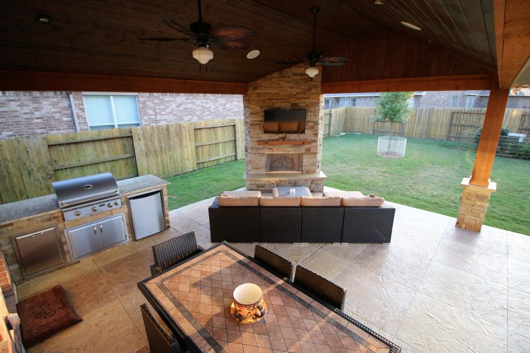 This project included a Patio Cover Addition, Outdoor Kitchen, Gas-Burning Fireplace, and Stamped Concrete walking surface with a custom pattern. The attention is immediately drawn to the Ledgestone fire place with a rustic cedar mantel. The Ledgestone flows continuously throughout the space, found on the base of the patio columns and outdoor kitchen. The kitchen sparkles with Stainless Steel appliances, containing storage compartments, refrigerator, and grill. Topped with Venetian Gold Granite, this cooking space provides ample counter space that is easily maintained. The overall appeal of this Outdoor Living area remains beautifully traditional, with cedar-trimmed columns and beams. Also, though it has custom features, this addition is built to look original to the home with matching paint, shingles, gutters, and framing materials. The elaborate, pre-stained Tongue and Groove ceiling is quite an attractive feature to this patio cover, and the recessed lighting illuminates the evening. The fans provide adequate air-flow and the sound system keeps the patio atmosphere in tune.