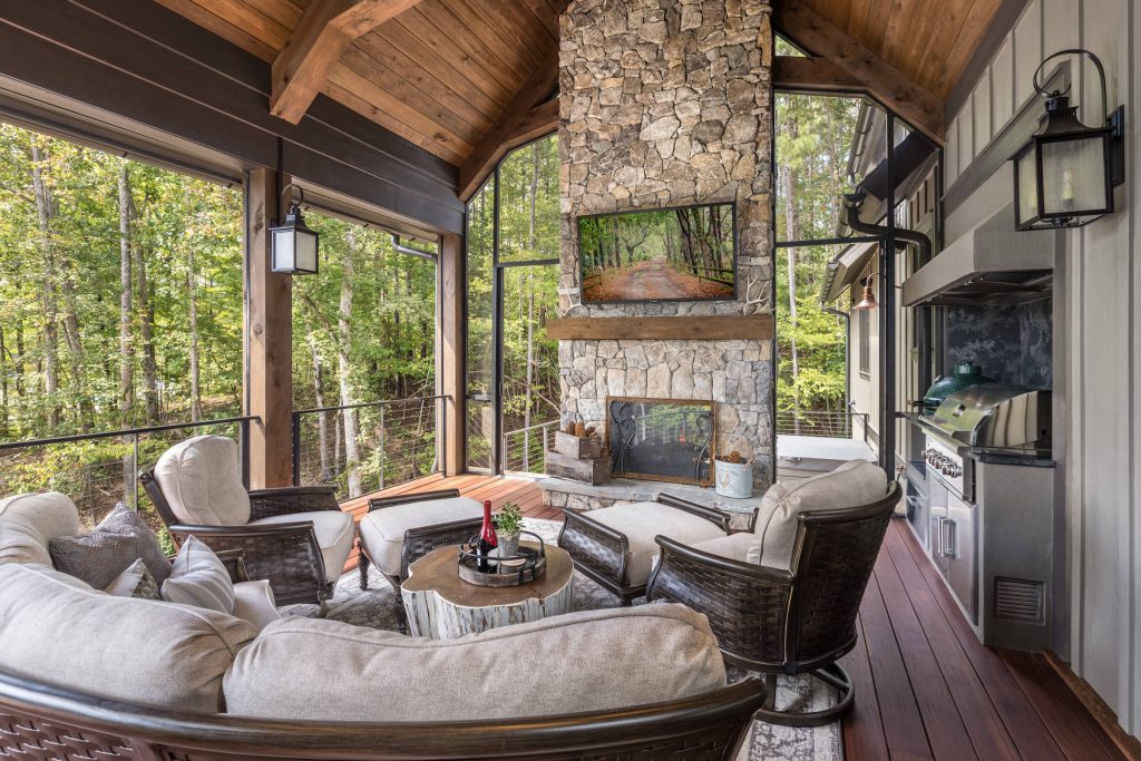 expansive covered porch with stunning lake views, features large stone fireplace, tv and a grilling station