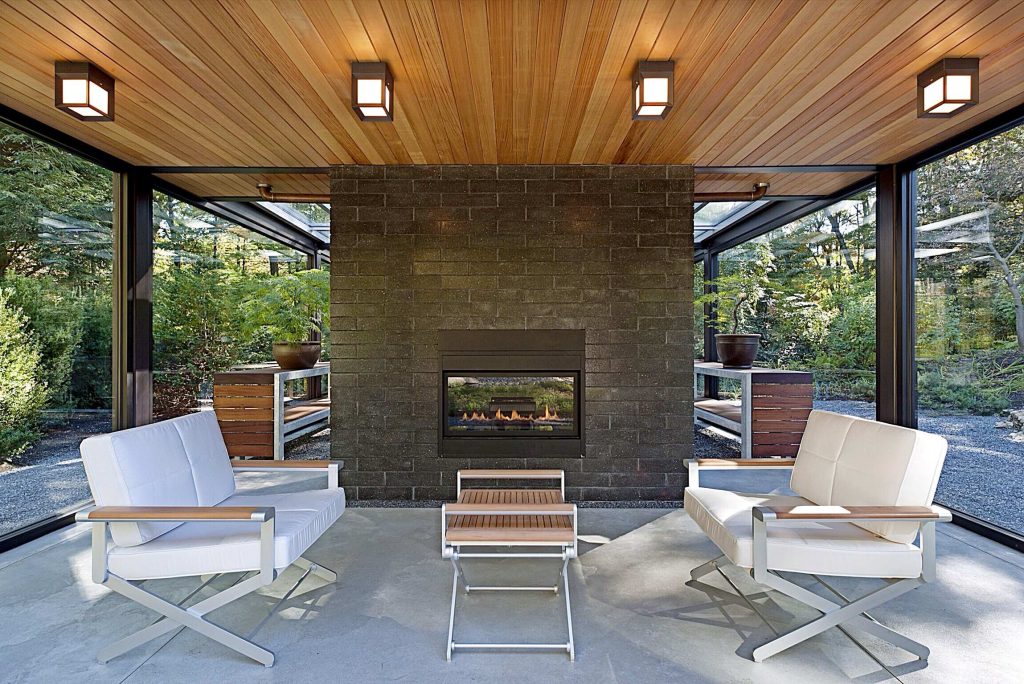 Modern glass house set in the landscape evokes a midcentury vibe. A modern gas fireplace divides the living area with a polished concrete floor from the greenhouse with a gravel floor. The frame is painted steel with aluminum sliding glass door. The front features a green roof with native grasses and the rear is covered with a glass roof. Photo by: Gregg Shupe Photography