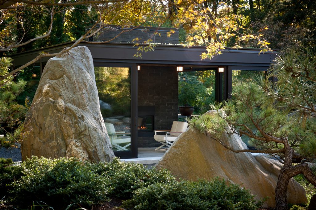 Modern glass house set in the landscape evokes a midcentury vibe. A modern gas fireplace divides the living area with a polished concrete floor from the greenhouse with a gravel floor. The frame is painted steel with aluminum sliding glass door. The front features a green roof with native grasses and the rear is covered with a glass roof. Photo by: Gregg Shupe Photography