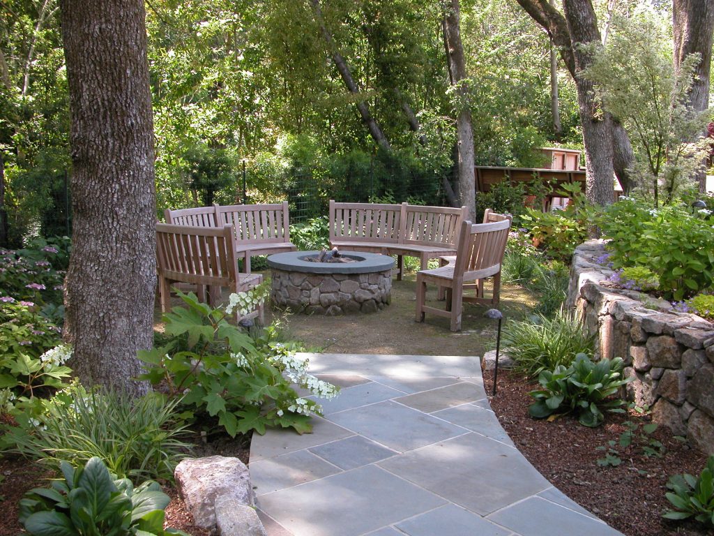 A stone fire pit with circular seating with teak benches photo by Galen Fultz