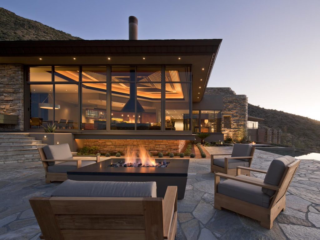 Evening view of cantilevered living room from pool patio. Painted steel fire pit with granite top, quartzite paving and wall stone, copper fascia, painted steel fascia at cantilevered slab edge. Bill Timmerman Photography