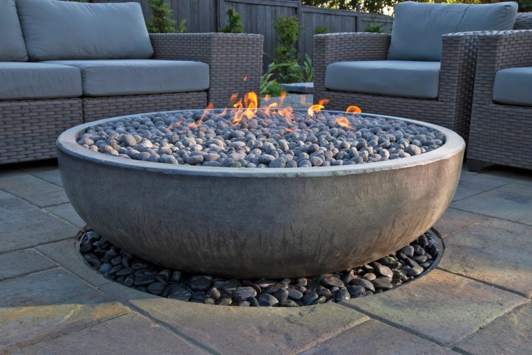 This spacious, multi-level backyard in San Luis Obispo, CA, once completely underutilized and overtaken by weeds, was converted into the ultimate outdoor entertainment space with a custom pool and spa as the centerpiece. A cabana with a built-in storage bench, outdoor TV and wet bar provide a protected place to chill during hot pool days, and a screened outdoor shower nearby is perfect for rinsing off after a dip. A hammock attached to the master deck and the adjacent pool deck are ideal for relaxing and soaking up some rays. The stone veneer-faced water feature wall acts as a backdrop for the pool area, and transitions into a retaining wall dividing the upper and lower levels. An outdoor sectional surrounds a gas fire bowl to create a cozy spot to entertain in the evenings, with string lights overhead for ambiance. A Belgard paver patio connects the lounge area to the outdoor kitchen with a Bull gas grill and cabinetry, polished concrete counter tops, and a wood bar top with seating. The outdoor kitchen is tucked in next to the main deck, one of the only existing elements that remain from the previous space, which now functions as an outdoor dining area overlooking the entire yard. Finishing touches included low-voltage LED landscape lighting, pea gravel mulch, and lush planting areas and outdoor decor.