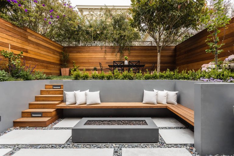 View of rear yard included custom-colored concrete walls, pavers, riverstone and a built-in bench around a firepit. Sliding Glass wall system by Nanawall. All exterior lighting by Bega. Catherine Nguyen Photography