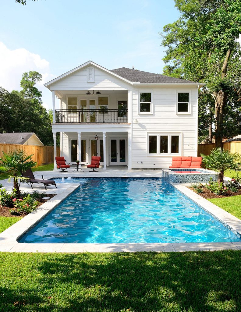 spill-over spa, rectangle pool, fountain, pavers, tiled spa, balcony, white siding, red cushions, tropical, lounge chair, grass, plant beds, wood fence, covered patio, blue pool tile