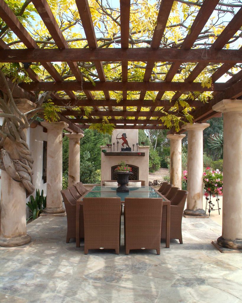 Dining under the pergola can be enjoyed year round at this San Diego residence. The columns, wood members, and vines come together to create an ideal al fresco dining location. The outdoor fireplace heightens the ambience in this special gathering space. The large woven dining set seats up to 12 for outdoor dinner parties.Credits: Hamilton-Gray Design, San Diego by Hamilton-Gray Design, Inc. | Fire Pits|Backyard Design|Outdoor Living Spaces|Landscape Design|Backyard Ideas|Landscaping|Landscaping Ideas|Landscape Installation|Fire Feautures|Fire Pit