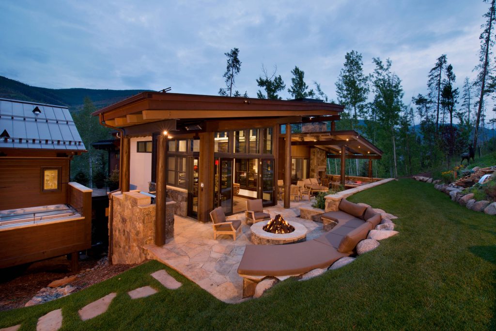 Example of a large mountain style backyard stone patio design in Denver with a fire pit and a roof extension